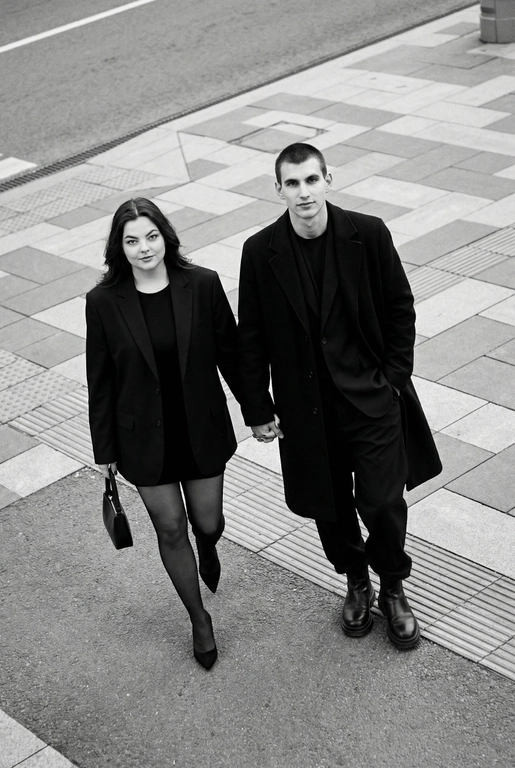 Черно-белая художественная фотография, ультрареализм, 8K, профессиональная съёмка; (оба): в кадре мужчина и женщина; каждый персонаж жёстко привязан к своему загруженному референсу, лица используются напрямую, без генерации, усреднения, подмены или смешения. Вид сверху под углом. Они идут по городской улице, держась за руки; шаг в движении, эффект «пойманного кадра». Смотрим вверх в камеру, выражение спокойное, уверенное, отстранённое.
Полностью чёрные образы modern classic: женщина — оверсайз-пиджак, короткое платье/юбка, плотные колготки, остроносые каблуки, маленькая сумка; мужчина — длинное пальто, свободный костюм, массивные ботинки.
Фон: асфальт, плитка, тактильная дорожка, геометрия.
Контрастный свет, мягкие тени, высокая детализация тканей.
Стиль: black & white, cinematic, high fashion, editorial, minimalism, street photography.
Качество: ultra high resolution, sharp focus, film grain, без ретуши.