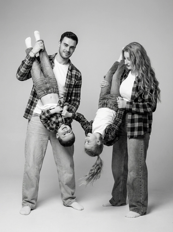     Создай, не меняя черты лица, перенеси их в точности с референса, без изменений. Студийный черно-белый семейный портрет четырех человек, изображающий радостный и игривый момент. Монохромный (черно-белый), с высокой контрастностью и мягким, равномерным освещением студии.Полная семья мужчина, женщина , мальчик 12 лет, девочка 9 лет, на однотонном фоне. Родители стоят, держа мальчика и девочку, обнимая их двумя руками за ноги, позы в динамике, дети игриво свисают вниз головой. Мальчик дегает девочку за волосы, девочка, смотрит на мальчика. Вертикальный кадр. В центре — отец, обнимающий сына за ноги, висящего вниз головой, и смотрит в кадр,  женщина , держит дочь за ноги, также висящую вниз головой.
Вся семья одета в гармонирующие наряды в белых и клетчатых тонах. 
белые футболки , голубые оверсайз джинсы, и клетчатые рубашки.  Волосы женщины волнистые, волосы девочки собраны в хвост. Однотонный, светлый (белый или очень светло-серый), студийный фон.
Мягкое студийное освещение, равномерно освещающее фигуры, с легкими тенями, подчеркивающими форму.На уровне глаз, немного снизу.
