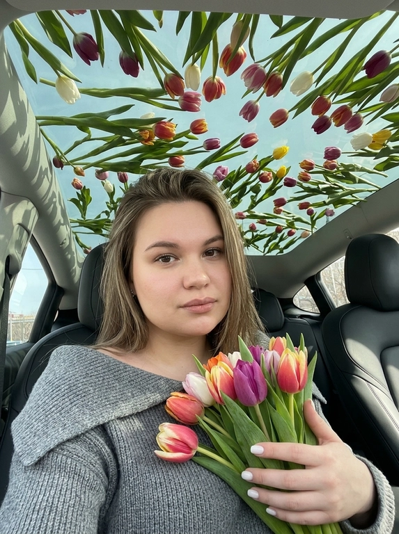 Ультрареалистичная фотография женщины, сидящей в современном автомобиле с большой панорамной стеклянной крышей. На коротких ногтях маникюр молочного цвета. Она сидит, делая селфи и держит букет тюльпанов (разные цвета). Естественный макияж.

Над панорамной крышей раскинулся густой полог из тюльпанов (разных цветов и сортов), покрывающий все небо. Тюльпаны хаотично лежат на всей поверхности стеклянной крыше (обязательно лежали на поверхности). Мягкий естественный солнечный свет пробивается сквозь тюльпаны, создавая красивые тени внутри автомобиля. Кинематографическое освещение, высокая детализация, роскошная лайфстайл-фотография, 8K. Не меняй пол, возраст, внешность, цвет волос.

Какой будет образ на фото?: На ней серый вязаный джемпер с широким отворотом, который носится открытыми плечами.