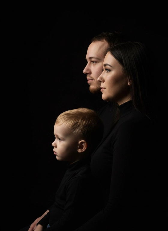 Профессиональный студийный портрет с низким контрастным светом. Головы расположены строго в одну линию, каскадом. боковой профиль, взгляд влево. У всех видны только головы и немного плечи. Черный фон. Черная одежда у всех. Люди занимают весь кадр. 3 человека. Порядок слева на право: отец-> мать-> сын