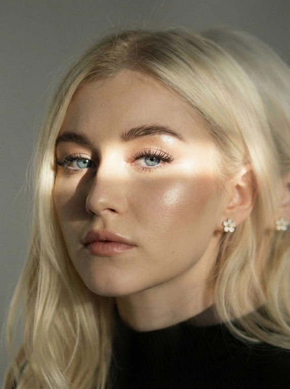 Кинематографический эффект с добавлением зерна. Ультрареалистичный, экстремально крупный портрет части лица девушки: на неё падает солнечный свет полосой, освещая глаза; её голова немного повёрнута в сторону. Тело подсвечено хайлайтером. Макияж лёгкий, с насыщенным хайлайтером; ресницы длинные, пышные. Она смотрит в камеру со спокойным, созерцательным выражением. Освещение мягкое, с лёгким акцентом на её лицо, создаёт нежные тени и подчёркивает черты. В ушах — серьги в виде белых цветов. Фон минималистичный и нейтральный, что усиливает спокойную и элегантную атмосферу. Фото смазанное, как будто сделано в движении, с двойной экспозицией.


Какая будет прическа?: Не изменять мою прическу.