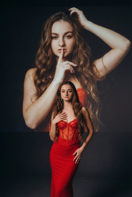 Создайте фотографию женщины в элегантной позе. На ней — слегка прозрачный облегающий красный корсет и длинное облегающее красное платье. Одной рукой она касается области груди, а другой — мягко опирается на бедро, что создаёт динамичную позу. Она смотрит с уверенностью и чувственностью. На ней простые серьги.
Эта женщина на переднем плане занимает меньшую часть высоты изображения. На ней — слегка прозрачный облегающий красный корсет и длинное облегающее красное платье.
Фон тёмный и минималистичный, с мягкой теневой проекцией той же женщины (в другой позе или в виде абстрактной фигуры) в верхней части изображения. Проекция — естественное цветное изображение женщины, которая представлена значительно крупнее и занимает большую часть верхней части фона. Она выглядит соблазнительно: одной рукой держит волосы, а палец другой руки прижала к губам, смотря при этом соблазнительным взглядом.
Не изменяй черты лица. Длинные волнистые волосы