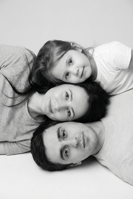 Создай чёрно-белый профессиональный студийный портрет на основе предоставленных фотографий. Съёмка сверху (top-down, overhead shot). Сохрани лица, возраст и индивидуальные черты людей.

Композиция: головы выстроены вертикальной  “башней” сверху вниз, по убыванию возраста в шахматном порядке.
Головы расположены близко друг к другу, как единая композиционная линия, но каждая имеет свою опору.
В кадре видны только головы и плечи.
Все смотрят в камеру, выражения мягкие и спокойные.

Одежда: однотонная, светлая или нейтральная.
Фон: чистый студийный, воздушный.
Стиль: high-key, мягкий ровный свет сверху, минимальные тени. Фотореализм, аккуратная текстура кожи, высокая детализация, 8K.Композиция «снизу вверх», шахматный порядок:
﻿﻿самый старший человек находится внизу, как мягкая подушка, его голова опирается на нейтральную студийную поверхность (например, плед или подушка);
следующие люди аккуратно и легко расположены на старшем человеке в шахматном порядке, их голова слегка приподнята, без ощущения давления; ﻿﻿

Несмотря на шахматное расположение, головы выстроены строго в одну вертикальную линию, взгляд в камеру.
Расположи их по убыванию возраста.

Видны только головы и плечи. Выражения мягкие, спокойные, нежные. Одежда однотонная, светлая или нейтральная, элегантная, без чёрного цвета.
Фон - чистый студийный, без пола и лишних деталей, создающий эффект «воздушного» портрета.
Стиль и освещение:
Студийная высококачественная чёрно-белая фотография (high-key).
Мягкий ровный свет сверху, минимум теней. Чистый фон; фотореализм, высокая детализация лиц, аккуратная текстура кожи; 8K.