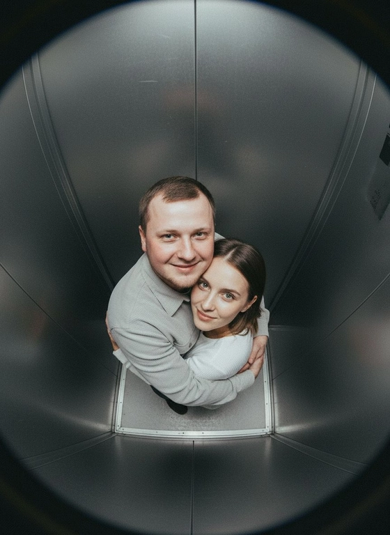 Используй предоставленные изображения и создай фото с двумя людьми в лифте с металлическими стенами. Цветовая гамма с преообладанием серых металлических оттенков. Кадр снят с максимально верхнего ракурса, люди будто заглядывают в камеру, их головы подняты наверх, взгляд в камеру. Легкий эффект fish eye. Реалистичное фото. Зернистость пленочного фото, насыщенные цвета, стиль фото y2k. Сохрани черты лица людей. Они обнимаются.