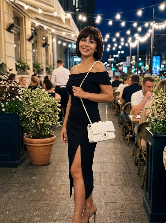 Фотореалистичное фото, снятое на iPhone, в эстетике elegant night outfit, feminine luxury vibe, Pinterest style. Кадр по бёдра или чуть ниже, модель находится на фоне стильного вечернего кафе или летней террасы. Фото выглядит естественно, как живой городской кадр без студийной постановки.

Модель с вечерним glam-макияжем: кожа с натуральной текстурой, длинные ресницы, подчёркнутые глаза, мягкий контуринг и розовые глянцевые губы. Выражение лица спокойное, мягкое, отстранённое и уверенное.

На модели через плечо белая стёганая сумка на цепочке. Образ элегантный, дорогой, вечерний и женственный.

Модель стоит в расслабленной fashion-позе: корпус слегка изогнут, одна рука заведена назад или лежит у талии, другая естественно держит сумку на плече. Голова немного наклонена в сторону, взгляд мягкий и уверенный. Поза плавная, женственная, с акцентом на талию, разрез юбки, сумку и силуэт.

На заднем плане вечерняя летняя терраса или вход в красивое кафе: мягкий тёплый свет лампочек сверху, цветы в кашпо, светлый декор, стеклянные панели, уютная ночная городская атмосфера. Фон слегка размыт, но читается как стильное модное заведение.

Освещение мягкое ночное, смешанное: тёплые лампы сверху и лёгкая холодноватая подсветка заведения на фоне. Свет не выглядит как студийный свет.

Цветокор cinematic: глубокие мягкие тени, сочетание голубовато-белых и тёпло-золотистых оттенков, лёгкий контраст, натуральные цвета, без чрезмерного HDR и без глянцевой рекламной обработки. Естественная текстура кожи, soft shadows, real life shot, iPhone photo, casual luxury lifestyle, no studio lighting, no CGI, no plastic skin, no over-retouching.

Какая будет одежда?: На модели элегантное платье миди с открытыми плечами и мягкой посадкой по фигуре. Ткань гладкая, плотная, без лишнего декора. Платье подчёркивает шею, ключицы и линию плеч, создавая дорогой женственный вечерний образ.

Какая будет прическа?: Не менять мою прическу