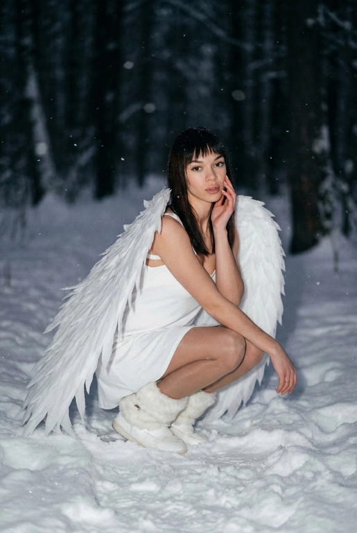  Создай фото человека на основе загруженной фотографии.
Белое платье без рукавов, пушистые белые сапоги, большие белые крылья, опущенные вниз, шире плеч.
Сидит на корточках на снегу, рукой касается щеки. На заднем плане заснеженный лес.
Ночная улица, тёмный размытый фон, вспышка.
Мягкое нечеткое фото: шум, зерно, лёгкое размытие, холодная атмосфера.