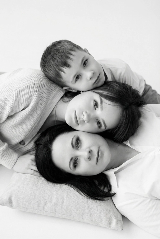 На основе предложенных фотографий, создай чёрно-белый профессиональный студийный портрет для этих людей, снятый сверху (top-down, overhead shot). Сохрани настоящие лица, возраст и индивидуальные черты людей.
Композиция «снизу вверх», шахматный порядок:
﻿﻿самый старший человек находится внизу, как мягкая подушка, его голова опирается на нейтральную студийную поверхность (например, плед или подушка);
следующие люди аккуратно и легко расположены на старшем человеке в шахматном порядке, их голова слегка приподнята, без ощущения давления; ﻿﻿

Несмотря на шахматное расположение, головы выстроены строго в одну вертикальную линию, взгляд в камеру.
Расположи их по убыванию возраста.

Видны только головы и плечи. Выражения мягкие, спокойные, нежные. Одежда однотонная, светлая или нейтральная, элегантная, без чёрного цвета.
Фон - чистый студийный, без пола и лишних деталей, создающий эффект «воздушного» портрета.
Стиль и освещение:
Студийная высококачественная чёрно-белая фотография (high-key).
Мягкий ровный свет сверху, минимум теней. Чистый фон; фотореализм, высокая детализация лиц, аккуратная текстура кожи; 8K.
