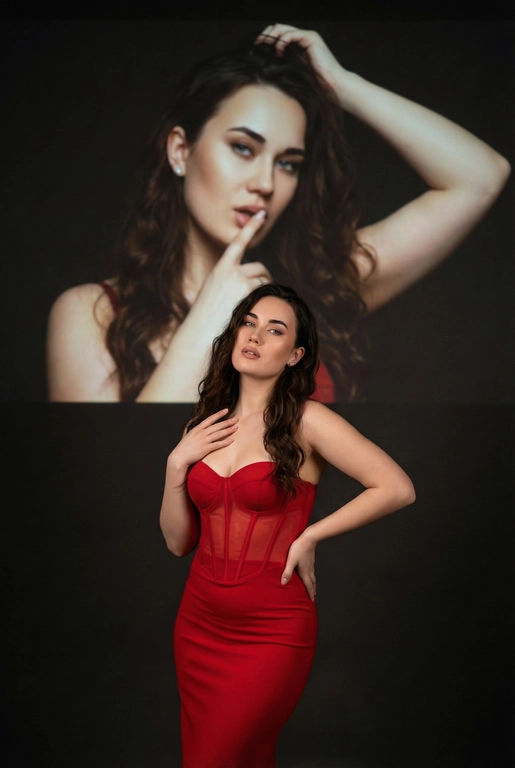 Создайте фотографию женщины в элегантной позе. На ней — слегка прозрачный облегающий красный корсет и длинное облегающее красное платье. Одной рукой она касается области груди, а другой — мягко опирается на бедро, что создаёт динамичную позу. Она смотрит с уверенностью и чувственностью. На ней простые серьги.
Эта женщина на переднем плане занимает меньшую часть высоты изображения. На ней — слегка прозрачный облегающий красный корсет и длинное облегающее красное платье.
Фон тёмный и минималистичный, с мягкой теневой проекцией той же женщины (в другой позе или в виде абстрактной фигуры) в верхней части изображения. Проекция — естественное цветное изображение женщины, которая представлена значительно крупнее и занимает большую часть верхней части фона. Она выглядит соблазнительно: одной рукой держит волосы, а палец другой руки прижала к губам, смотря при этом соблазнительным взглядом.
Не изменяй черты лица. Длинные волнистые волосы