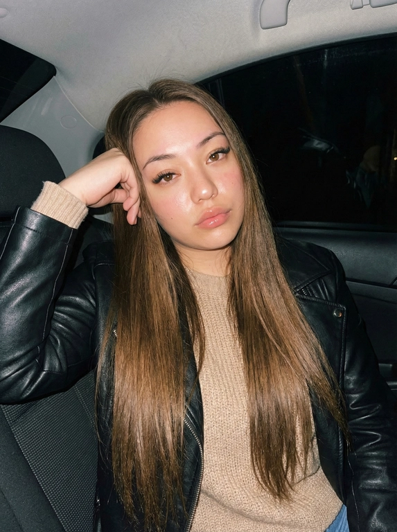   Создай изображение меня, максимально сохрани мою внешность.
Портрет молодой женщины, снятый ночью в машине со вспышкой.
Она сидит на заднем сиденье, слегка наклонившись вбок; правой рукой непринуждённо поддерживает голову и смотрит прямо в камеру — спокойно и уверенно.  Длина волос до пояса. Причёска, прямые волосы
Бежевый джемпер, а на нём кожаная куртка.
Фон тёмный, едва различимый; видны лишь лёгкие блики на поверхностях внутри автомобиля.
Стиль и эффекты:
эстетика Y2K;
мягкая вспышка;
проработка текстур (кожа и ткань);
лёгкое ретросияние;
мягкий эффект «песка»;
высокий блеск на губах и щеках;
тёплые тона с лёгким винтажным настроением....
