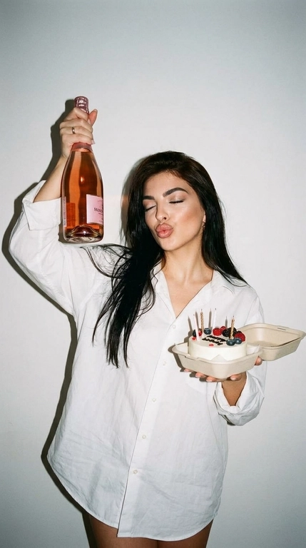 Ультрареалистичная фотография в эстетике Party Girl / Birthday Aesthetic, стилизация под случайный снимок на компактную цифровую камеру начала 2000-х.
 девушка празднует день рождения. На ней свободная белая рубашка оверсайз на пуговицах. В одной руке она высоко держит бутылку розового шампанского, в другой — небольшой бенто-торт со светлыми свечами и свежими ягодами.

Глаза закрыты, на лице игривое выражение с лёгким «поцелуйным» жестом губ. Не меняй прическу модели.

Съёмка со вспышкой прямо в камеру на фоне простой молочно-белой стены. Жёсткий свет создаёт характерную чёткую тень за фигурой, яркие блики на коже, волосах, бутылке и глазури торта. Атмосфера спонтанного домашнего праздничного снимка: немного несовершенная композиция, лёгкая зернистость, естественная текстура кожи, реалистичные отражения и мелкие детали.

Стиль: 2000s digital camera, lo-fi party aesthetic, candid snapshot, hard flash, authentic lifestyle photography, natural skin texture, realistic colors, high detail, 4K.

Без: студийной постановки, мягкого идеального света, пластиковой кожи, чрезмерной ретуши, CGI, мультяшности, искажённых рук и пальцев, лишних пальцев, деформированной бутылки или торта, артефактов текста, логотипов и водяных знаков.