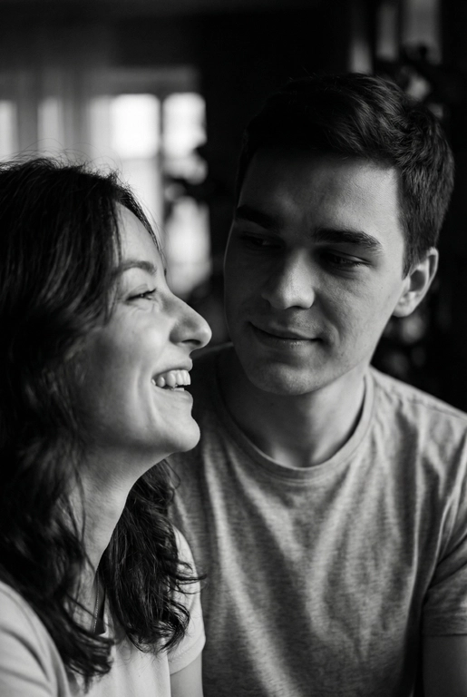   Сгенерируй Черно-белое фото, кинематографичная фотография пары, снятая крупным планом. девушка находится слева в кадре на переднем плане, повернута в профиль и смеется, не глядя на парня , парень справа на заднем фоне смотрит на глаза девушки задумчиво и влюбленно, с мягким, нежным, влюбленным выражением лица. свет падает сбоку, создавая мягкие тени на лицах и подчёркивая черты лица . фон размытый , темный , без четких деталей , создававший атмосферу уюта фотография выглядит как кадр из романтического фильма или личный момент пойманный камерой формат фото