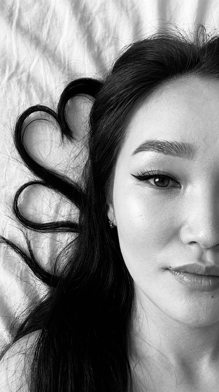 Фото снято на фронтальную камеру iPhone 16 Pro Max. Фотореалистичное чёрно-белое селфи девушки, лежащей на светлой слегка смятой простыне. крупный план. Камера расположена прямо над лицом. В кадре видна только половина лица, один глаз смотрит прямо в камеру.

Макияж выразительный и аккуратный, в эстетике clean soft glam: чёткие графичные чёрные стрелки с вытянутым эффектом, длинные густые ресницы с лисьим эффектом, хорошо оформленные брови с аккуратной укладкой наверх, мягкий контуринг, деликатный хайлайтер во внутренних уголках глаз, на скулах и спинке носа, губы с чётким контуром и мягким гладким финишем. Макияж выглядит безупречно, дорого и очень чисто.

Волосы естественно уложены на одну сторону вокруг головы, две крупные пряди случайно образуют два сердца, остальные волосы свободно и натурально лежат волнами. Мягкий естественный дневной свет из окна, лёгкие тени. Высокая детализация лица, чётко видны поры кожи, текстура губ, ресницы, брови и отдельные волоски. Волосы максимально детализированные, с естественным блеском и объёмом. Минималистичный кадр, светлая ткань с натуральными складками на фоне, без лишних предметов. Фото снято на фронтальную камеру iPhone 16 Pro Max.