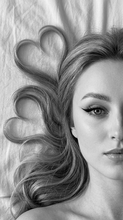 Фото снято на фронтальную камеру iPhone 16 Pro Max. Фотореалистичное чёрно-белое селфи девушки, лежащей на светлой слегка смятой простыне. крупный план. Камера расположена прямо над лицом. В кадре видна только половина лица, один глаз смотрит прямо в камеру.

Макияж выразительный и аккуратный, в эстетике clean soft glam: чёткие графичные чёрные стрелки с вытянутым эффектом, длинные густые ресницы с лисьим эффектом, хорошо оформленные брови с аккуратной укладкой наверх, мягкий контуринг, деликатный хайлайтер во внутренних уголках глаз, на скулах и спинке носа, губы с чётким контуром и мягким гладким финишем. Макияж выглядит безупречно, дорого и очень чисто.

Волосы естественно уложены на одну сторону вокруг головы, две крупные пряди случайно образуют два сердца, остальные волосы свободно и натурально лежат волнами. Мягкий естественный дневной свет из окна, лёгкие тени. Высокая детализация лица, чётко видны поры кожи, текстура губ, ресницы, брови и отдельные волоски. Волосы максимально детализированные, с естественным блеском и объёмом. Минималистичный кадр, светлая ткань с натуральными складками на фоне, без лишних предметов. Фото снято на фронтальную камеру iPhone 16 Pro Max.