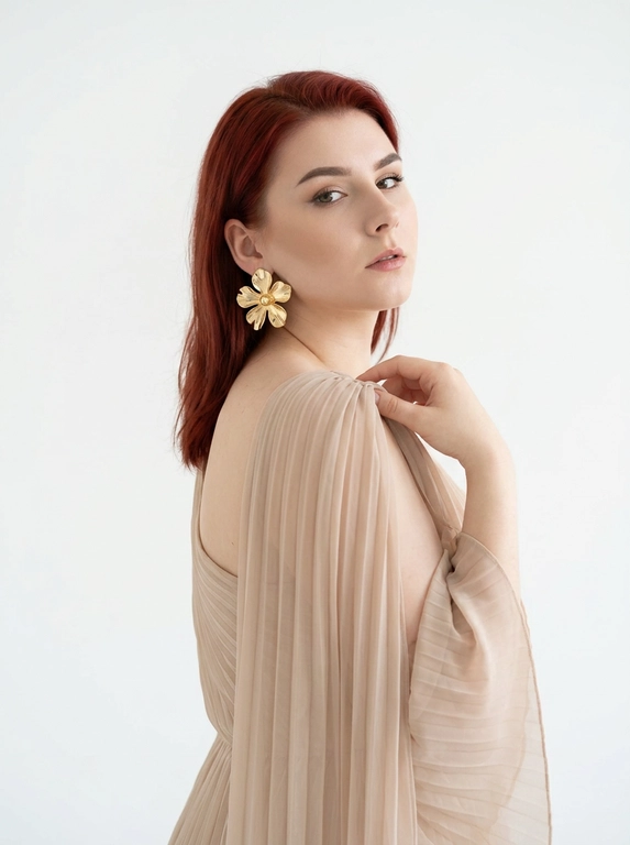 Студийный портрет женщины, выполненный в стиле fashion-съемки. Фон белый, без каких-либо отвлекающих деталей. Свет мягкий, рассеянный, создающий ощущение свежести и легкости. Цветовая гамма нейтральная, с преобладанием пастельных тонов.
На женщине надето платье из полупрозрачной плиссированной ткани . Платье открывает одно плечо. На ухе видна массивная золотая серьга в форме цветка.
Женщина стоит полубоком к камере, повернув голову назад через плечо. Взгляд направлен в камеру. Поза расслабленная и уверенная. Одна рука приподнята и частично придерживает ткань платья на плече.

Цвет платья: Платье светлого бежевого оттенка