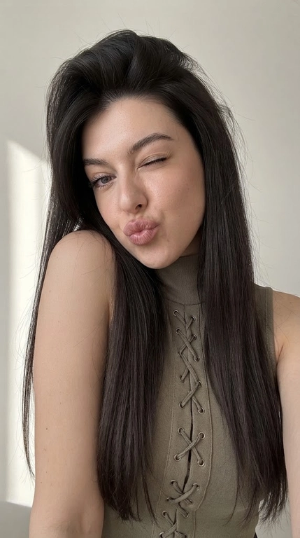 A hyper-realistic everyday photo taken on an iPhone 17. 9:16 AM
Without changing the woman's appearance, a close-up selfie of a young woman with very full lips and expressive foxy eyes. The woman tilts her head to one side, resting her cheek lightly on her shoulder, her lips pursed into a kiss, one eye winking, her gaze directed at the camera. The pose is playful and flirtatious.
The woman is wearing a khaki sleeveless turtleneck top with lacing down the chest to the solar plexus.
Her hair is very long, reaching to her waist, thick, shiny, and has volume at the roots.
The background is minimalist, light, with a soft shadow on the wall, creating a homely atmosphere.
Shot on an iPhone 16 Pro. The skin texture is natural, matte, velvety, with visible pores and a subtle glow on the protruding areas. Do not use strong HDR processing or full facial retouching.
High detail in the face and clothing.
Don't blur the background.
Close-up shot, focus on the face and emotions.
Soft evening lighting, no flash.
Rich girl selfie atmosphere, clean luxury aesthetic.
Selfie!