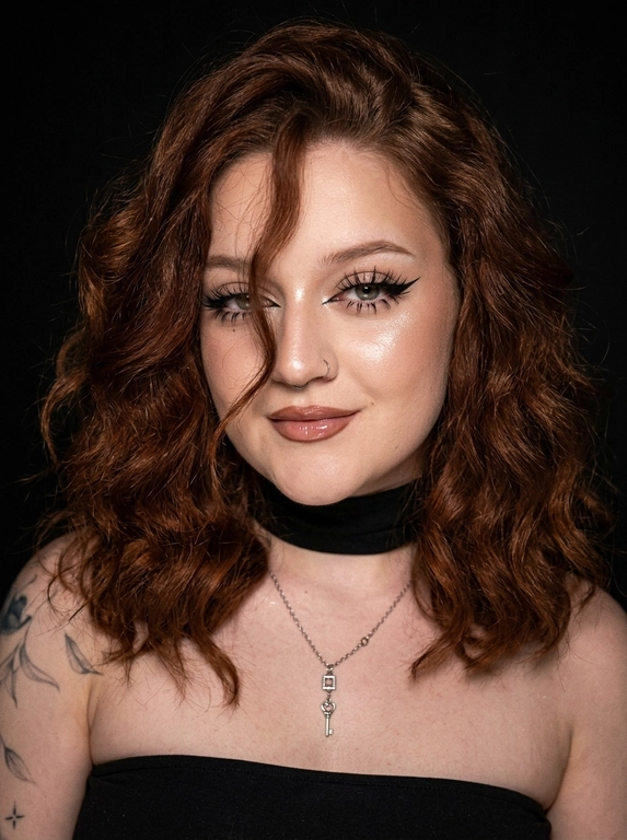 Крупный план лица женщины в стиле «высокой моды». Элегантный макияж: глаза с длинными острыми чёрными стрелками, длинные густые ресницы с эффектом «лучики», нижние ресницы также прокрашены. Хайлайтер во внутренних уголках глаз и на скулах. Губы слегка приоткрыты в лёгкой ухмылке, с лёгким блеском и светло-коричневым карандашом по контуру. Голова наклонена в сторону,  На ней чёрный топ из тканевого материала без бретелек. Тело и зона декольте подсвечены хайлайтером, на шее чёрная ткань. Высокая детализация текстур кожи, одежды и волос. Черты лица полностью сохранены, как на референсном фото. Фон чёрный, студийный, вокруг темнота, лицо освещено яркой лампой. 8K, тёмный минималистичный фон без лишних деталей. Гиперреализм, добавить зерно.

Какая будет прическа?: Волосы густые уложены в пляжные локоны, локон волос падает на лицо.