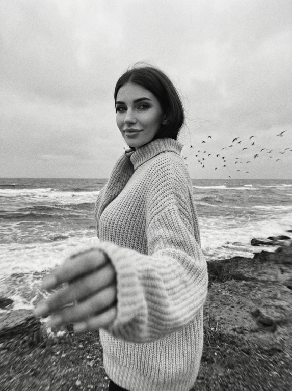Создай портрет, не меняя черты лица. Черно-белая фотография в стиле ретро: человек стоит на морском побережье, в полупрофиль, смотрит нежно в камеру, легкая улыбка на лице, одет(а) в светлый оверсайз вязаный свитер с высоким воротником. На переднем плане — размытая рука в движении (motion blur), на заднем плане — море с волнами и стая птиц в небе, пасмурное небо. Сильная зернистость пленки, винтажная эстетика, атмосфера свободы, эффект размытия в движении, эстетика.



