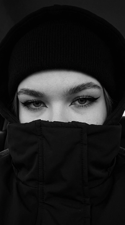 Не меняя внешности женщины с фото, перед нами крупный план её лица, частично скрытого под чёрной шапкой-бини, капюшоном и чёрной курткой с высоким воротом, которые обнимают нижнюю часть лица, оставляя видимыми только выразительные глаза.

Очень близкое селфи на iPhone 16, горизонтальный кадр, видно только глаза и брови, взгляд направлен прямо в камеру. Фото цветное, сильно затемнённое, с глубокими тенями, мягким контрастом и холодной приглушённой цветокоррекцией. Чёрные элементы одежды остаются насыщенными и глубокими, кожа сохраняет естественный оттенок без пересветов и искусственного сглаживания.

Веки полуприкрыты, создавая томный, тяжёлый и дерзкий взгляд. Стрелки большие, острые, дерзкие, с чёткими графичными линиями. Ресницы длинные и пушистые. Брови строго очерчены и подчеркнуты тёмным оттенком. Взгляд направлен прямо в камеру, создавая атмосферу загадочности и напряжённости.

Свет падает мягко и равномерно, но остаётся очень приглушённым, делая главный акцент на глубине взгляда. Волосы, видимые лишь частично, слегка выбиваются из-под шапки.

Фон очень тёмный, приглушённый, с минимальным количеством цветовых деталей и без ярких отвлекающих оттенков. Общая цветовая гамма холодная, глубокая и кинематографичная, с лёгким уклоном в серо-графитовые и нейтральные тона.

Стиль кадра кинематографичный, с высокой глубиной теней, реалистичной текстурой кожи и ткани, без глянцевой ретуши, без эффекта пластика и без ИИ-сглаживания. Фотореалистичное изображение, высокая текстурная детализация, разрешение 8K. Фото снято на iPhone 16.


Фото в чёрно-белом или в цвете?: Стиль кадра чёрно-белый