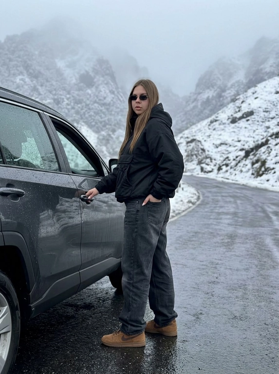 Не менять черты лица человека с исходного фото. Человек рядом с стоит рядом с машиной, машина на горной дороге, дорога мокрая от тумана, машина в каплях от тумана. Чёрный анорак Planta Rosa, маленькие чёрные солнцезащитные очки без оправы, мешковатые серо-чёрные джинсы с низкой посадкой, длинные, коричневые замшевые кроссовки Nike Dunk, руки в карманах. Машина без номеров. Фон — гиперреалистичные заснеженные холмы Мегхалайи, без зелени, туманные горы, пасмурный мягкий дневной свет, без размытия, без изменения лица или позы, без дополнительных объектов. Фото снято на iPhone 17 Pro, без фильтров на лице, без ретуши, перспектива снизу, формат 9:16, машина как на исходном фото, фон не размывать, притемнённая экспозиция, открывает дверь машины, стоит спиной, смотрит в камеру, будто сейчас сядет за руль.


Какая будет машина?: Toyota RAV4 2.0 CVT, 2020