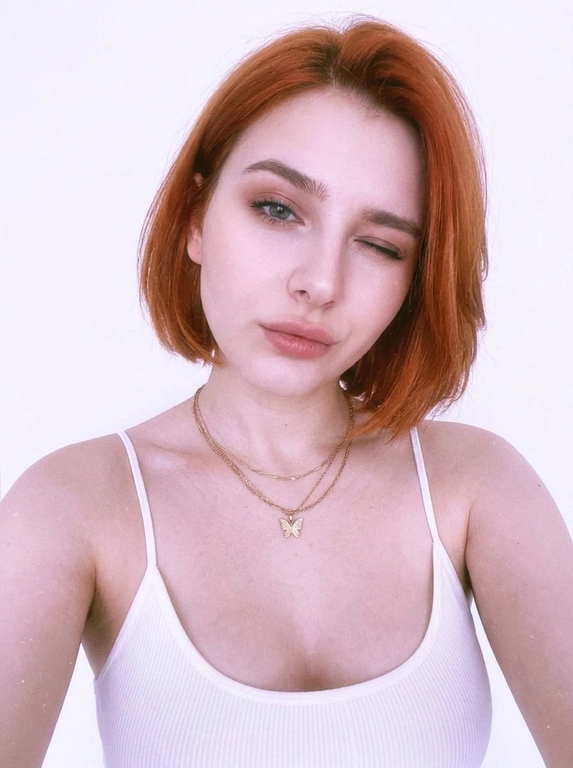 Vertical close-up portrait in the style of a natural selfie: a woman with her head tilted and a soft playful expression, one eye squinted or closed, gaze directed at the camera.
Expressive full lips, neat eyebrows, and soft makeup with an emphasis on the lips and eyes are noticeable on the face. There are thin chains around her neck, one with a small butterfly pendant.
The clothes are a white ribbed tank top with thin straps, revealing the shoulders and upper chest. The background is almost completely white, empty and minimalistic, like a light wall, without unnecessary objects.
The light is very soft, diffused, slightly overexposed, with a cool pink and purple hue, creating a gentle, slightly dreamy atmosphere.
The composition is close and intimate, the frame is cropped around the shoulders and chest, with emphasis on the face. The camera is at face level, creating the feeling of taking a picture from a phone. Light graininess, a gentle loss of detail in the highlights, natural, fashionable, slightly vintage aesthetic.



Причёска: Не менять прическу