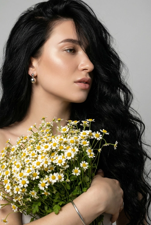 Создайте ультрареалистичный портрет, не меняя черты лица, крупным планом 3/4, с мягкой, освещённой кожей, атласной отделкой и естественным блеском, где женщина изображена в профиле. Спокойное и чувственное выражение лица, губы слегка полуоткрыты. Она носит серебряные серьги-шары и простой серебряный браслет на запястье.
Фон нейтральный, в светло-сером тоне, с тёмным, целенаправленным низким угловым освещением, которое подчёркивает контур лица, текстуру кожи и объём волос. Стиль редактирования — высокая мода, чёткий фокус 8K, реалистичная текстура, изысканная и элегантная атмосфера.


Длинные волнистые волосы покрывают часть лица объёмными локонами, выпадающими на лицо и плечо. 

Какие будут цветы?: Держит в руках огромный букет ромашек