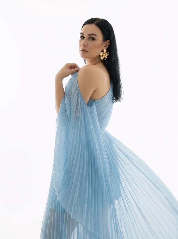 Студийный портрет женщины, выполненный в стиле fashion-съемки. Фон белый, без каких-либо отвлекающих деталей. Свет мягкий, рассеянный, создающий ощущение свежести и легкости. Цветовая гамма нейтральная, с преобладанием пастельных тонов.
На женщине надето платье из полупрозрачной плиссированной ткани . Платье открывает одно плечо. На ухе видна массивная золотая серьга в форме цветка.
Женщина стоит полубоком к камере, повернув голову назад через плечо. Взгляд направлен в камеру. Поза расслабленная и уверенная. Одна рука приподнята и частично придерживает ткань платья на плече.

Цвет платья: Платье нежно голубого оттенка