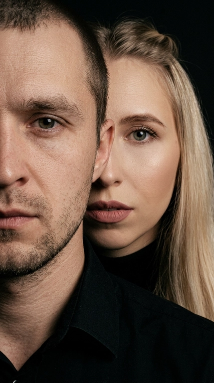 Не менять лицо. Нельзя менять цвет волос. Создайте кинематографическую фотографию. Сохраняйте точную структуру лица, пропорции и естественную асимметрию. Экстремальный портрет крупным планом. У них чёрная одежда. Чёрный фон.
Плотная обрезка: видна только часть лица мужчины (половина лица) Женщина, расположенная прямо за ним. Ее лицо частично скрыто за его головой/плечом Сильная многослойная композиция (мужчина на переднем плане, женщина на заднем плане)
Мужчина, обращенный вперед слегка повернулся сторону. Женщина стоит очень близко позади него.
Женщина стоит очень близко позади него. Губы мягко прижаты или слегка приоткрыты взгляд в камеру. Эмоциональное напряжение вместо романтики. У женщины безупречный легкий скульптурный макияж и матовыми губами пыльная роза. 

Какая будет прическа у женщины?: Не менять прическу