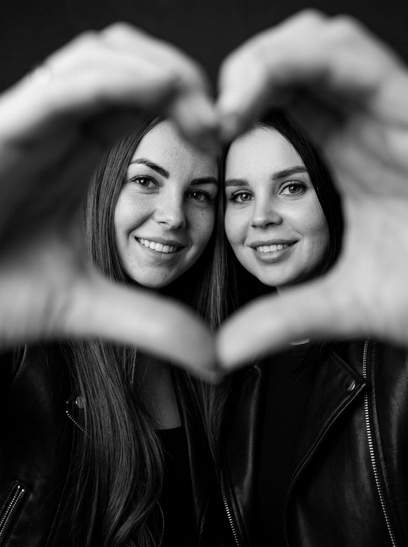 Ultra-realistic editorial photography of a smiling couple in a romantic and cinematic composition. The couple is centered in the background of the image, looking directly at the camera with a spontaneous, happy, and natural expression. In the foreground, extremely close to the lens and slightly out of focus, the couple’s hands form a heart shape perfectly framing their faces.

The composition creates strong visual depth, with sharp focus on the eyes and faces inside the heart formed by the hands. The hands occupy a large portion of the foreground, artistically blurred around the edges, creating a sophisticated cinematic effect.

Intimate, emotional, and elegant aesthetic inspired by modern perfume campaigns and premium lifestyle editorials. Soft studio lighting with delicate contrast and natural shadows. Minimalistic dark blurred background.

The couple wears minimalistic black leather jackets and sophisticated dark clothing. Genuine expressions, strong emotional connection, contemporary romantic atmosphere. Hyper-realistic skin texture, visible pores, detailed hair strands, authentic human appearance.

Black and white photography, rich tones, deep blacks, and soft highlights. 85mm lens, shallow depth of field, cinematic portrait photography, luxury editorial style, ultra detailed, hyper realistic, 8K.