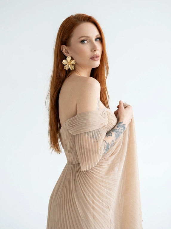 Студийный портрет женщины, выполненный в стиле fashion-съемки. Фон белый, без каких-либо отвлекающих деталей. Свет мягкий, рассеянный, создающий ощущение свежести и легкости. Цветовая гамма нейтральная, с преобладанием пастельных тонов.
На женщине надето платье из полупрозрачной плиссированной ткани . Платье открывает одно плечо. На ухе видна массивная золотая серьга в форме цветка.
Женщина стоит полубоком к камере, повернув голову назад через плечо. Взгляд направлен в камеру. Поза расслабленная и уверенная. Одна рука приподнята и частично придерживает ткань платья на плече.

Цвет платья: Платье светлого бежевого оттенка
