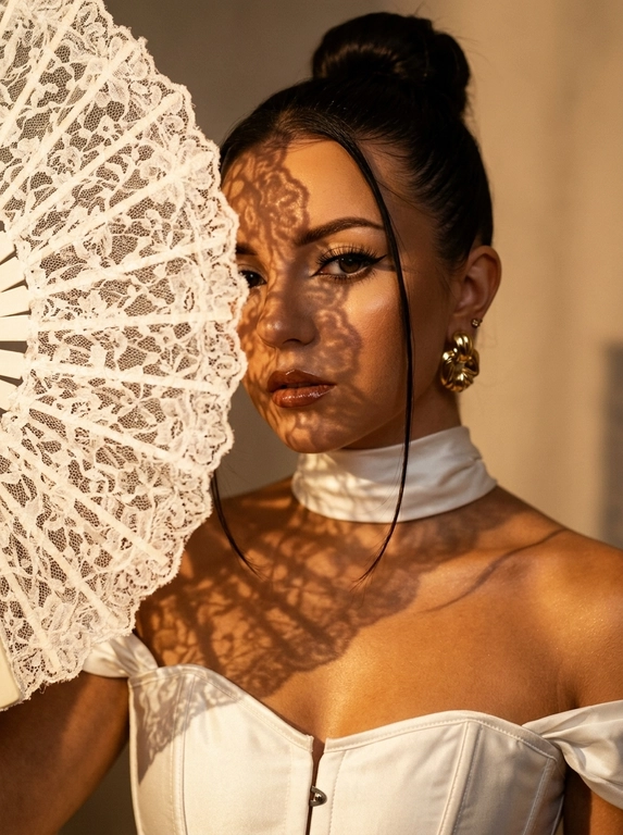 Ultra realistic beauty editorial portrait. Крупный портрет модели: лицо, шея и плечи, лёгкий наклон камеры. Белый кружевной веер частично закрывает лицо, создавая чёткие lace shadows на щеке, глазе, шее и ключице.
Белый структурный корсет с открытыми плечами и плотный satin neck wrap, плотно облегающий шею.  Макияж: sharp eyeliner, длинные ресницы, glossy brown lips, сияющая бронзовая кожа с натуральной текстурой.
Тёплый направленный свет, глубокие тени, золотистый glow, крупные золотые серьги, cinematic contrast, subtle film grain, Vogue aesthetic, RAW realism, ultra detailed 8K, no plastic skin.

Какая будет прическа?: Волосы — sleek high bun с тонкой прядью у лица.