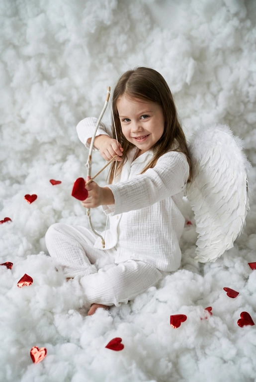 Использовать реальные черты лица человека с референса, естественную текстуру кожи и настоящий цвет и длину волос. Личность должна оставаться неизменной.

Y2K. Сказочная сцена с купидоном, сфотографированная как реальный момент.
Человек сидит среди плотных, пушистых белых облаков, которые полностью заполняют передний, средний и задний план, образуя бесшовную белую среду с многослойной глубиной.

Поза вполоборота: корпус слегка повернут вбок, одно плечо выдвинуто вперед, как будто человек натягивает и отпускает небольшой лук с красной стрелой в форме сердца; руки подняты с легким напряжением, указывающим на движение при выстреле.

Несмотря на поворот тела, голова повернута к объективу, взгляд направлен прямо в камеру. Выражение лица радостное и игривое, с мягкой улыбкой.

Наряд — простая белая пижама: свободная рубашка и брюки из муслина.
На спине — крылья из белых перьев, настоящие и фактурные, с четкими бликами по краям каждого пера.

Вокруг объекта в воздухе хаотично летают только конфетти в форме сердечек — маленькие красные сердечки из глянцевой фольги, расположенные на разном расстоянии: часть в переднем плане, часть растворяется среди облаков.

Без рассеянного света, без мягкого свечения, без студийного глоу.
Текстура кожи реалистичная и детализированная, без сглаживания и без фильтров.
Тонкая зернистость, волшебное, но искреннее ощущение Y2K-редакции — выглядит как фотография, а не визуализация.