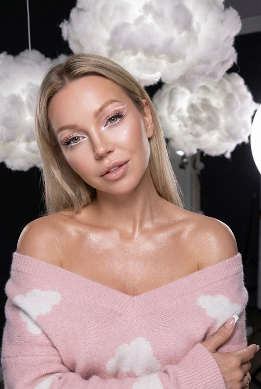 Крупный план лица девушки в стиле «высокой моды». Элегантный макияж глаза с длинными острыми нежно розовые двойные изогнутые стрелки, длинные густые ресницы эффект лучики, нижние густо ресницы накрашены белым и белый каял карандаш на нижнем веке белый Хайлайтер во внутренних уголках и скулах. Губы слегка приоткрыты в легкой ухмылке в легком блеске. Голова наклонена в сторону. На ней пушистый дорогой кашемировый нежно розовый свитер с белыми облаками плечи открыты.
За ней свисают объемные пушистые облака из ваты подсвеченные белым изнутри. Тело и декольте подсвечены хайлайтером и шиммером. Высокая детализация текстур кожи, одежды и волос. Черты лица-полностью сохранены как на референсном фото.
Ногти френч квадрат длинные.
На фоне светлая большая бьюти студия, вокруг темно, ее лицо освещено яркой лампой. Не менять свою прическу