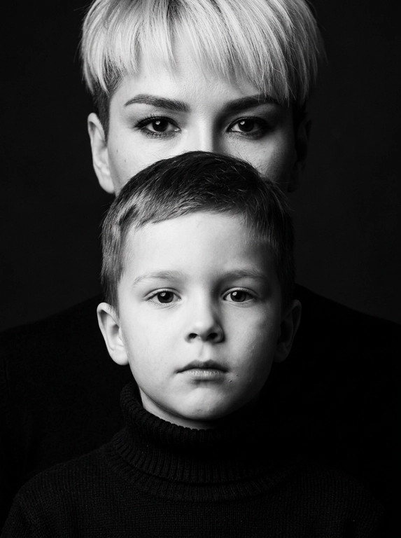 Сохрани реалистичную текстуру кожи и пор, избегая пластического сглаживания.
Сохрани естественные пропорции.
Друг за другом.
Создай портрет крупным планом, не изменяя черт лица.
Перенеси изображение точно так, как это показано на прилагаемых фотографиях.
Черно-белый, выразительный студийный портрет крупным планом, сфокусированный на лицах Взрослого человека и ребенка.
Взрослый стоит на заднем плане, его рот закрывает полностью голова ребенка, видны только глаза и лоб.
Ребенок на переднем плане, смотрит прямо в камеру с важным выражением лица. Он одет в черную водолазку с горлом.
Фон темный.
Освещение мягкое, но эффектное, с
акцентом только на чертах лица, расположение высокое, а объект съемки кинематографичный.
Внешность и черты лица строго сохранены по сравнению с эталонной фотографией.