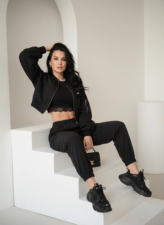 > Не меняя внешности женщины с фото, перед нами раскрывается динамичная и стильная сцена, в которой актриса в полной мере выражает уверенность и современную элегантность. Она сидит на белом ступенчатом выступе, развернувшись к зрителю фронтально и слегка наклонив голову вправо, в сторону своей поднятой руки, локоть которой опирается на голову, создавая эффектный изгиб. Средняя часть тела женщины обнажена, демонстрируя подтянутый живот, который контрастирует с черной короткой топовой майкой с тонкой кружевной отделкой по краю – эта текстура нежно выделяется на фоне гладкого материала остальной одежды. Её верхняя одежда представляет собой чёрный укороченный бомбер с объемными рукавами, которые собираются в манжеты, придавая образу спортивное настроение с утонченным акцентом. Ткань этого бомбера выглядит мягкой и матовой, с мелкими деталями, такими как карман с застёжкой и небольшой белый логотип, тиснённый на нем, придавая изделию индивидуальность. Брюки также черные, из легкой ткани с эластичной талией и манжетами на щиколотках, что создает эффект спортивной элегантности и свободы движения. Левая нога согнута в колене и покоится на подиуме, тогда как правая вытянута вперед на пол, что придает композиции большую глубину и динамичность. Обувь женщины представляет собой массивные чёрные кроссовки Balenciaga,  придавая образу дерзость и утонченность. В руках она удерживает небольшую черную сумку с золотистой пряжкой, лежащую возле её поднятой ноги, добавляющую детали образу без отвлечения внимания от самой фигуры. Волосы длинные, чёрного цвета с мягкими волнами, аккуратно уложены, обрамляя лицо и создавая нежный контраст на фоне монохромного наряда. Освещение мягкое, равномерно подчеркивающее контуры тела и лица, создавая теплую и приглушённую атмосферу, без резких теней, что добавляет кадру ощущение легкости и чистоты. Фон минималистичен, почти полностью белый, с едва заметной архитектурной аркой слева и текстурированным цилиндрическим объектом, частично скрытым тенью, который усиливает композиционную глубину и не отвлекает от центрального персонажа. Взгляд женщины устремлён прямо в камеру, выражая непоколебимую уверенность и лёгкую игривость, при этом её черты лица сохраняют ясность и индивидуальность без излишних эмоций. Эта сцена наполнена балансом между расслабленной элегантностью и энергией, визуально подчеркиваемой контрастом тёмной одежды и светлого окружения, создавая по-настоящему кинематографическое настроение, фотореалистичное изображение, высокая текстурная детализация, высокое качество, разрешение 8K.