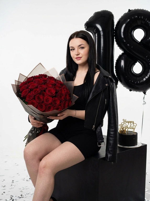 Максимально реалистичная фотография в стиле luxury birthday editorial, элегантная и торжественная студийная съемка премиального уровня.
Полный рост. женщина сидит на матовом черном кубе, уверенно и расслабленно удерживая перед собой большой роскошный монобукет цветов в упаковочной бумаге. Взгляд направлен прямо в камеру, легкая полуулыбка создает спокойное и уверенное настроение кадра.
Макияж вечерний и элегантный: с мягкой растушевкой, густые ресницы.
Одежда: черный облегающий ромпер с короткими шортами, подчеркивающий силуэт. Поверх небрежно накинута черная кожаная куртка-косуха на одно плечо. Мягкая фактура кожи с естественными бликами и складками материала.
Локация: минималистичная белая фотостудия. На заднем плане расположены большие черные фольгированные шары в форме цифр. На полу рассыпано серебристое конфетти, рядом с кубом стоит небольшой черный праздничный торт с золотой надписью «Happy Birthday» и декоративной короной.
Освещение: профессиональный студийный свет с мягким рисующим источником спереди и легким контровым светом, создающим объем и мягкие естественные тени.
Съемка на полнокадровую камеру, объектив 50mm. Модель, монобукет и торт находятся в идеальном фокусе, задний план слегка размыт.
Гиперреалистичная текстура кожи без пластиковой ретуши: видны поры, естественный микрорельеф кожи, текстура рук и ног, натуральные блики на коже и волосах.
Высокая детализация лепестков цветов, упаковочной бумаги букета, текстуры кожи куртки, отражений на фольгированных шарах и фактуры торта.
RAW photo, ultra photorealistic, luxury birthday editorial, studio photography, natural skin texture, realistic lighting, subtle film grain, high detail, 8K, vertical 2:3.
Без AI-артефактов, пластикового эффекта кожи, пересветов, HDR, неестественных цветов, деформации рук, ног и пальцев.

Шары в форме цифр: 18

Какие цветы в букете?: Темные красные розы