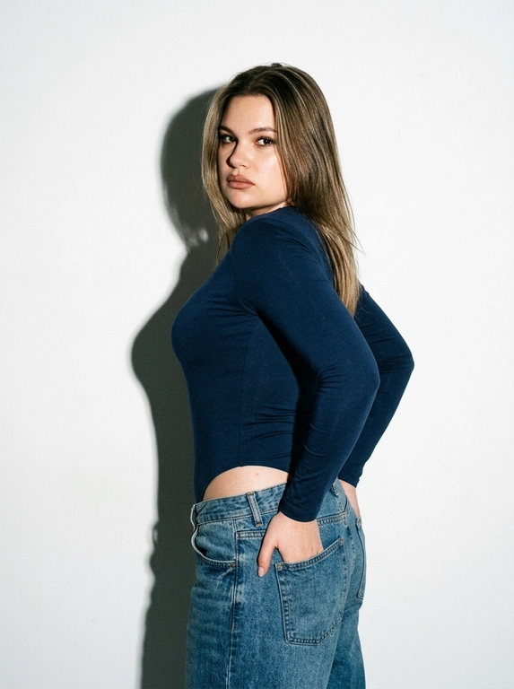 Ультрареалистичная фотография женщины, Эстетика пленочной фотографии 90-х годов, внешний вид Pentax.
K1000 + Kodak Tri-X 400, но в цвете, сильное зерно пленки, высокая контрастность, жесткая прямая студийная вспышка, которая создает четкую тень на белой стене.
Минималистская студия, чистый белый фон. Одежда: темно-синий боди с длинными рукавами, низ джинсы свободные низкая посадка. Макияж: карандаш для губ, накрашенные ресницы. Крупный план, стоит полубоком, руки строго в ЗАДНИХ карманах джинс, взгляд через плечо.
Кинематографическая цветовая градация, редакционная статья в винтажном журнале 90-х годов, четкие детали, реалистичная текстура кожи, зернистость аналоговой пленки, фотография со вспышкой.